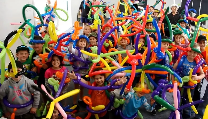 A big group of kids holding up the colorful balloon creations they twisted