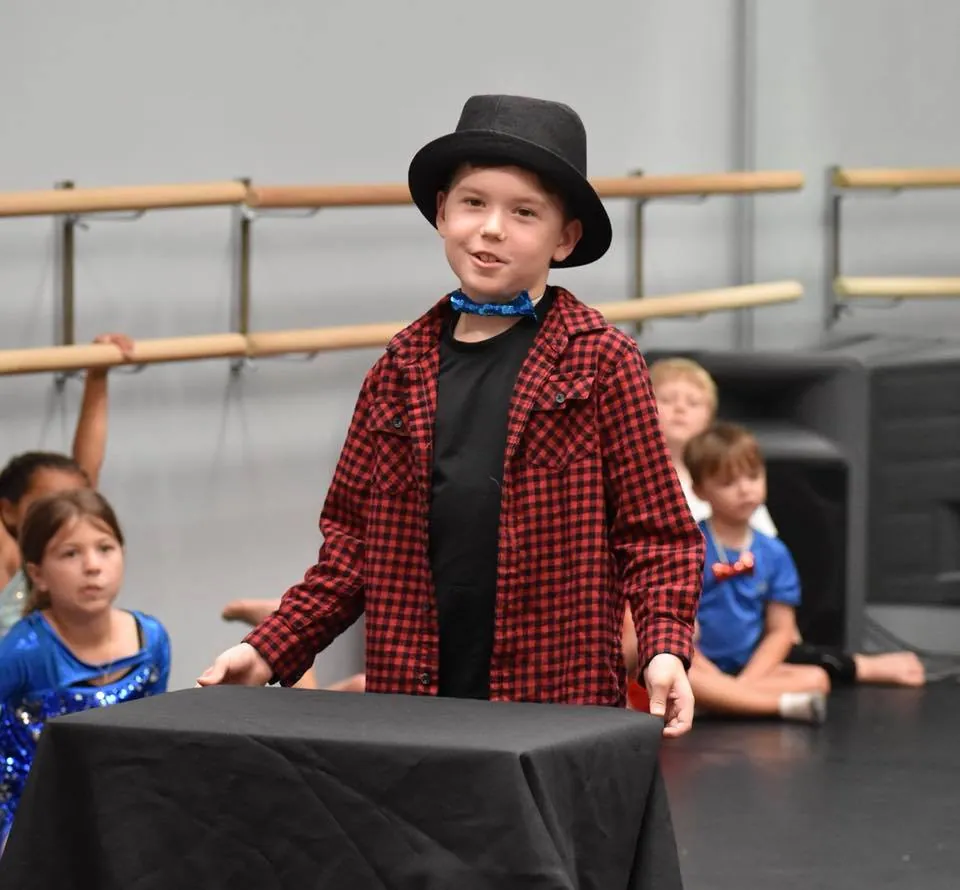 A young volunteer in a top hat performing a trick in front of other kids