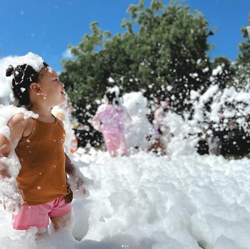 A child standing waist-deep in foam on a sunny day