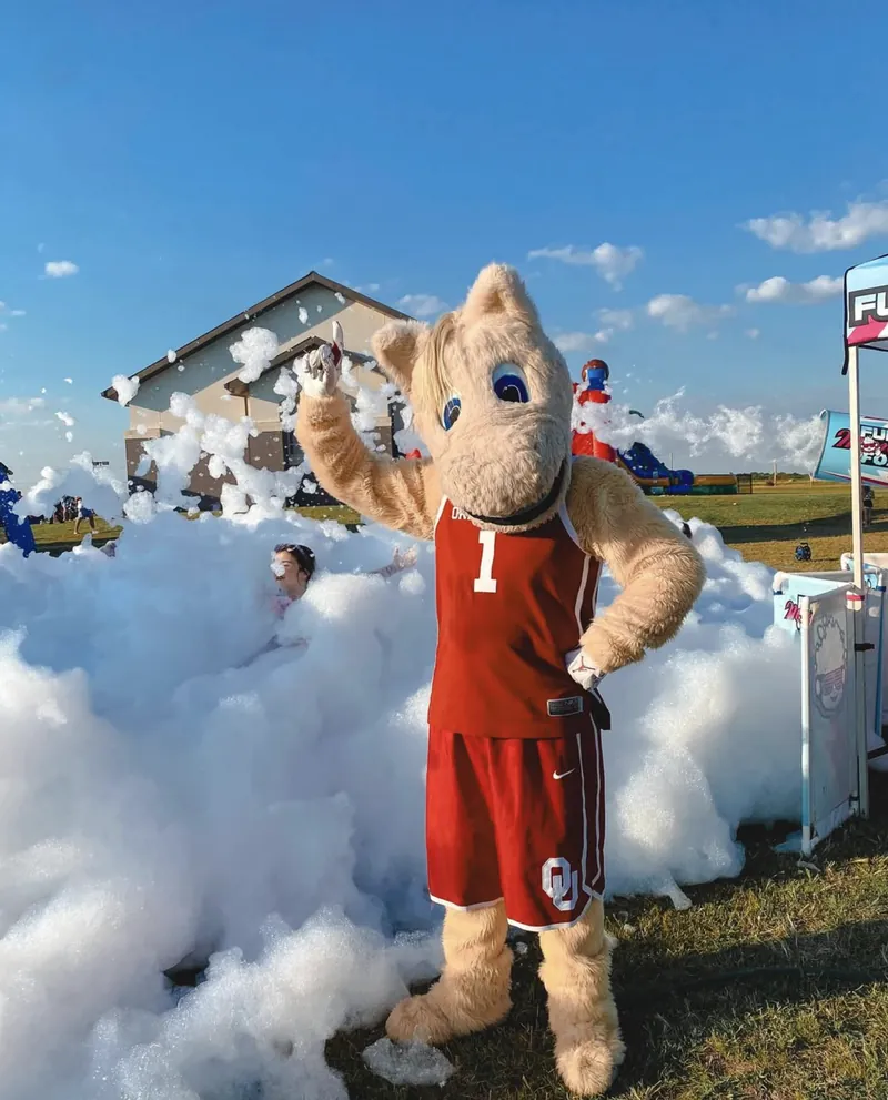 A costumed mascot standing in a field of foam at an outdoor foam party
