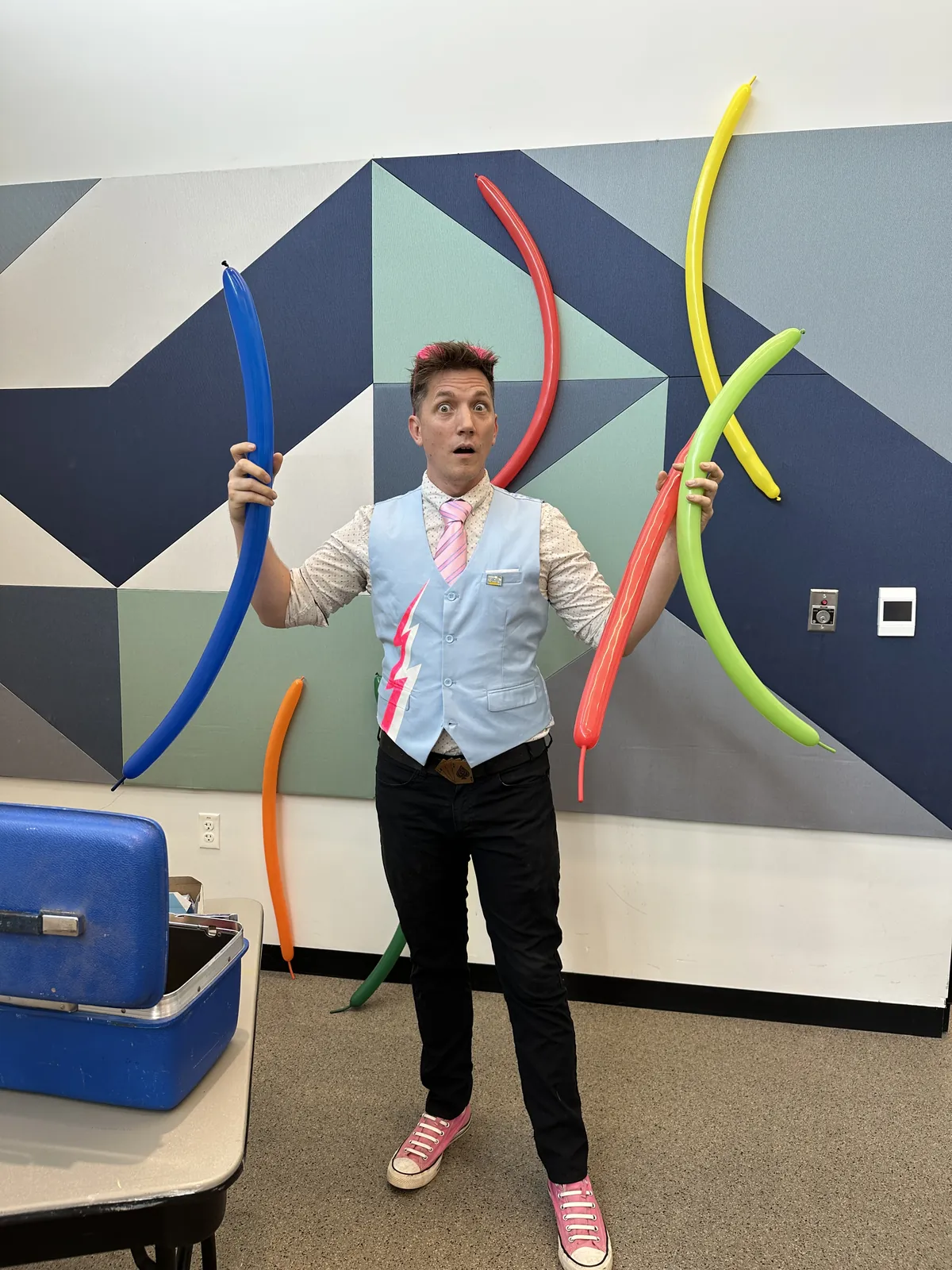 Joe Coover holding long twisting balloons in a library program room