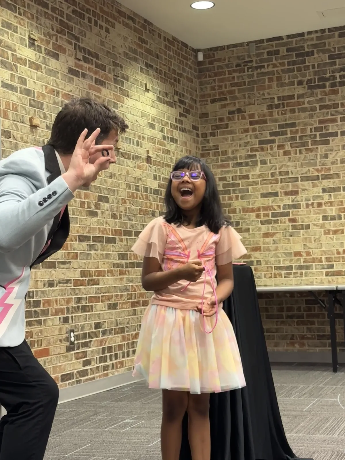 A girl laughing in amazement as Joe Coover performs a magic trick beside her