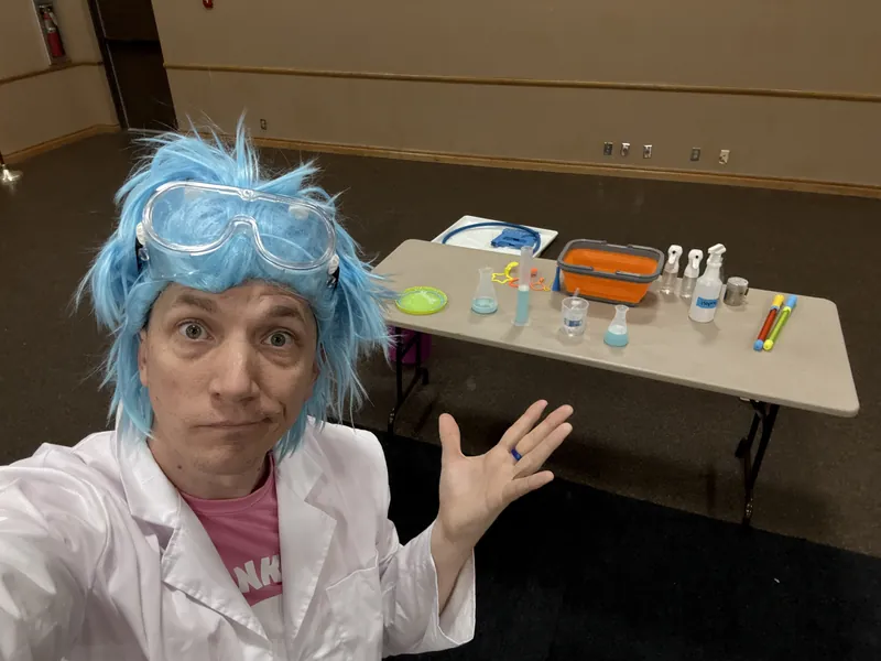 Joe Coover in costume as Professor Buckets, with a blue wig, goggles and a lab coat